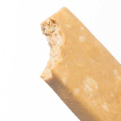 A close-up image of unwrapped and partially bitten White Chocolate Macadamia Cookie Dough bar.