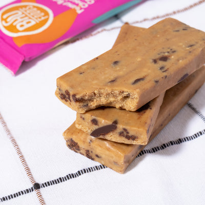 A close-up image of three unwrapped one partially bitten Peanut Butter Chocolate Chip Cookie Dough bars beside an individually wrapped bar.