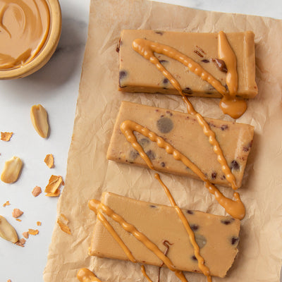 A close-up image of three unwrapped Peanut Butter Chocolate Chip Cookie Dough bars with some peanut butter swirl on top of the bars and peanuts on the side.