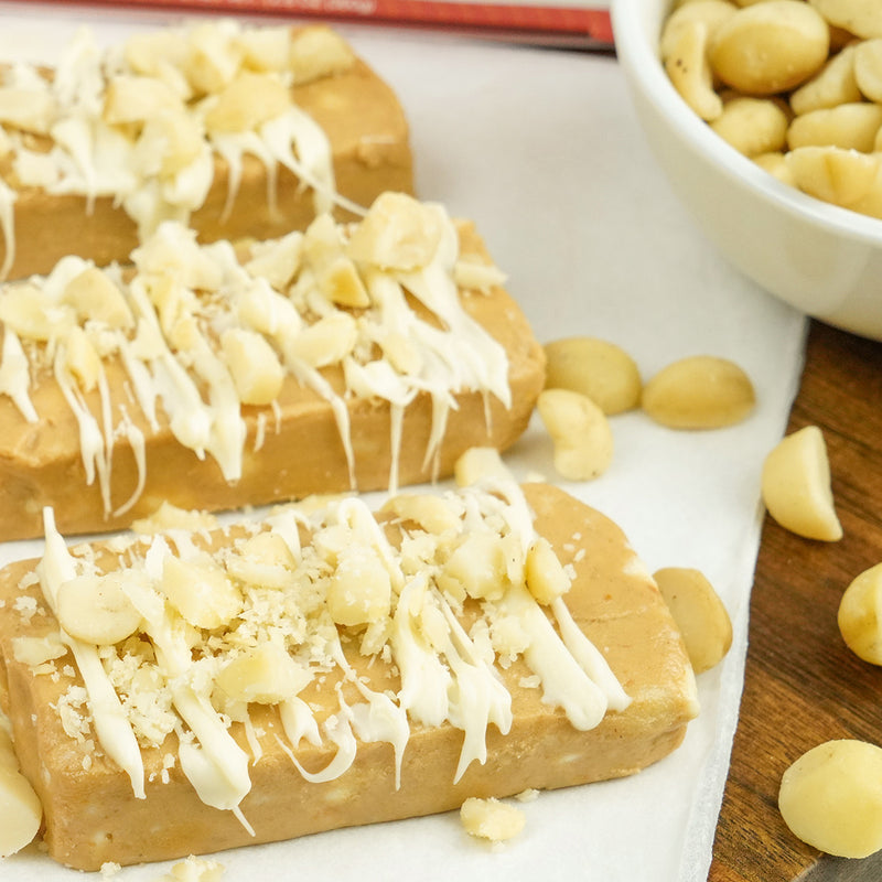 A close-up image of three unwrapped White Chocolate Macadamia Cookie Dough bars with some macadamia nuts and white chocolate swirl on top.