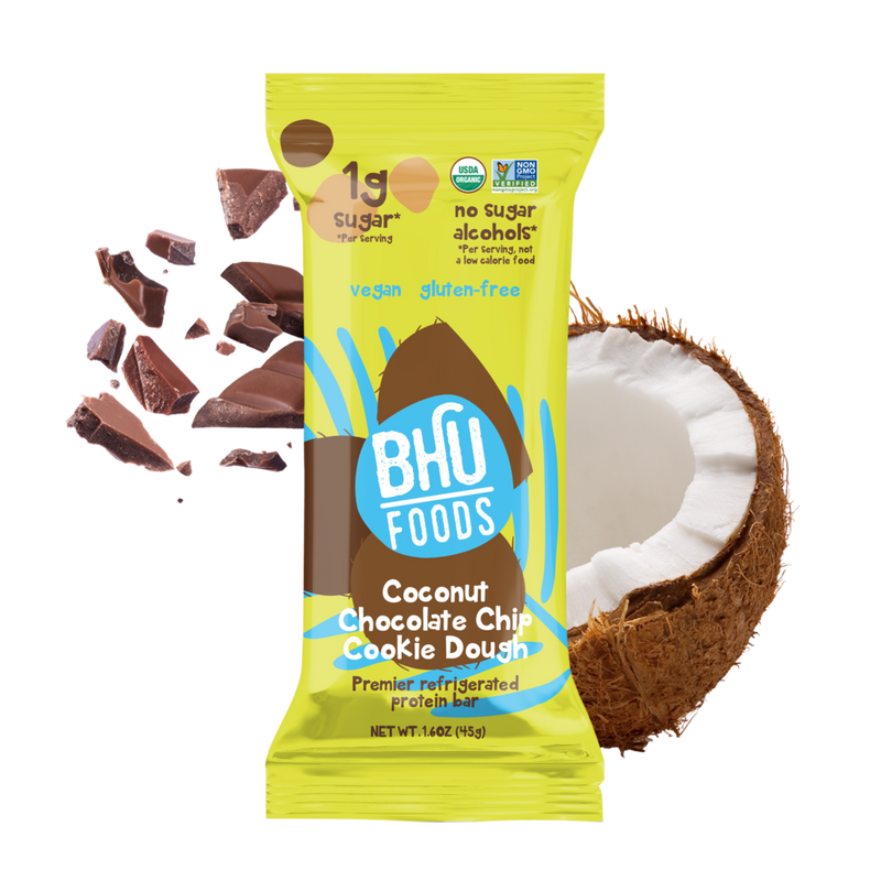 An individually wrapped Coconut Chocolate Chip Cookie Dough Premier Refrigerated Protein Bar with some chocolate and coconut behind it.