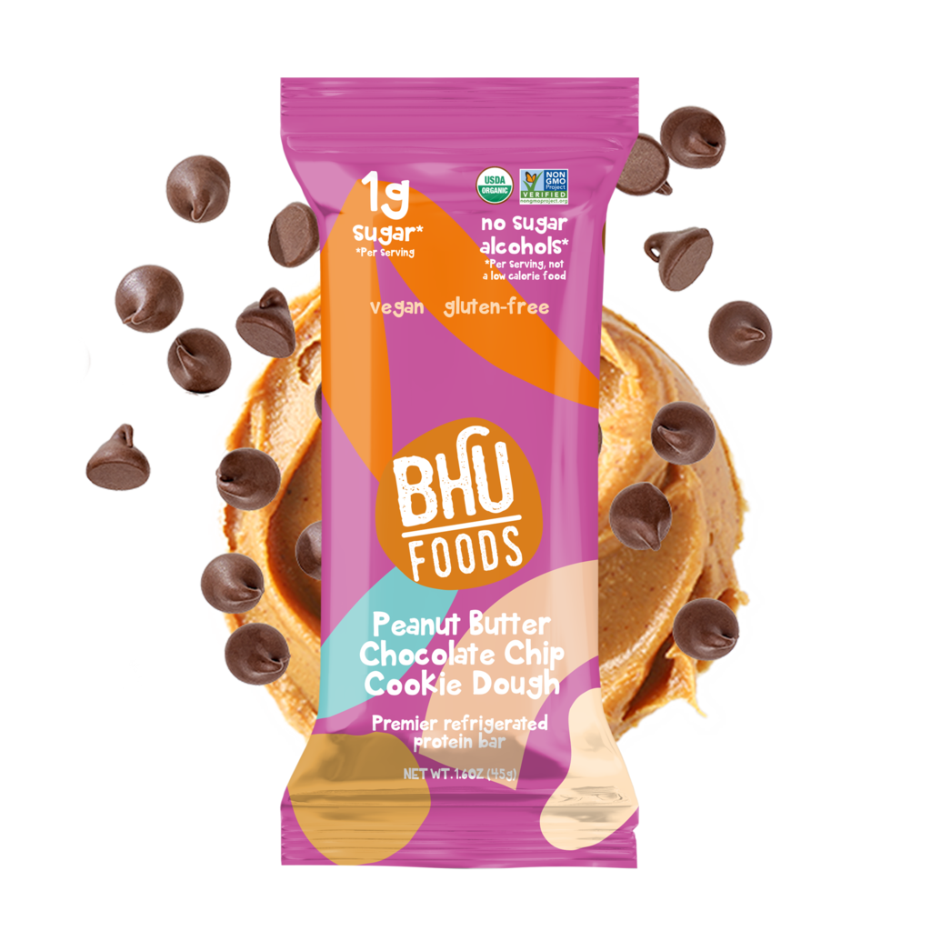 An individually wrapped Peanut Butter Chocolate Chip Cookie Dough Premier Refrigerated Protein Bar with some chocolate chips and peanut butter behind it.